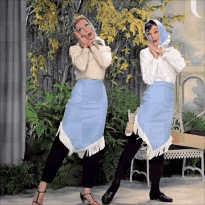 Two Women Are Standing Next To Each Other And One Is Wearing A Blue Skirt With Fringe GIF