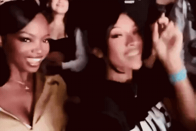 Two Women Are Standing Next To Each Other In A Crowd At A Party And Smiling . GIF