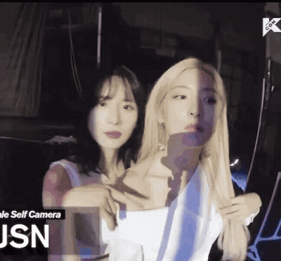 Two Women Are Standing Next To Each Other In A Dark Room . One Of The Women Is Taking A Selfie With Her Phone . GIF