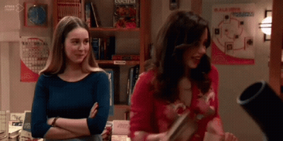 Two Women Are Standing Next To Each Other In A Room With A Bookshelf . GIF