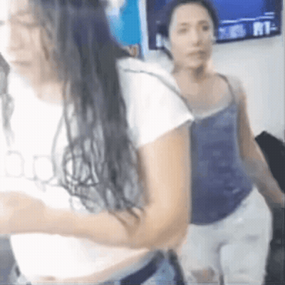 Two Women Are Standing Next To Each Other In A Room With A TV On The Wall Behind Them . GIF