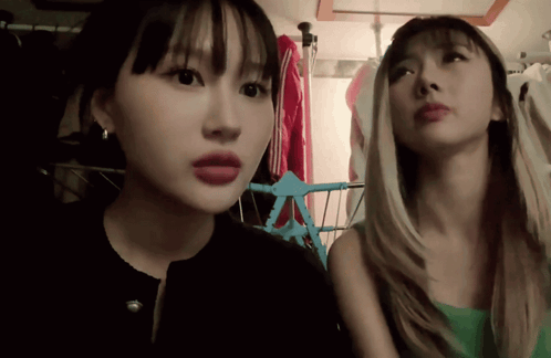 Two Women Are Standing Next To Each Other In A Room With Clothes Hanging On A Rack GIF