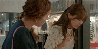 Two Women Are Standing Next To Each Other In A Store And One Of Them Is Holding Her Chest . GIF