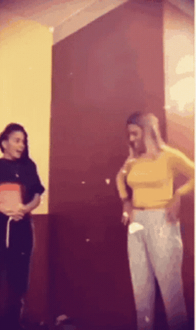 Two Women Are Standing Next To Each Other In Front Of A Red Wall . GIF