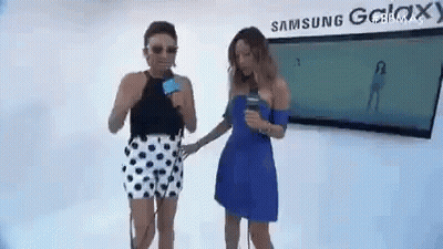 Two Women Are Standing Next To Each Other In Front Of A Sign That Says Samsung Galaxy . GIF