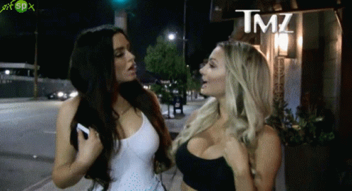 Two Women Are Standing Next To Each Other In Front Of A Sign That Says Tmz On It GIF