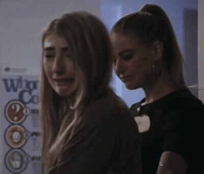 Two Women Are Standing Next To Each Other In Front Of A Sign That Says Who GIF