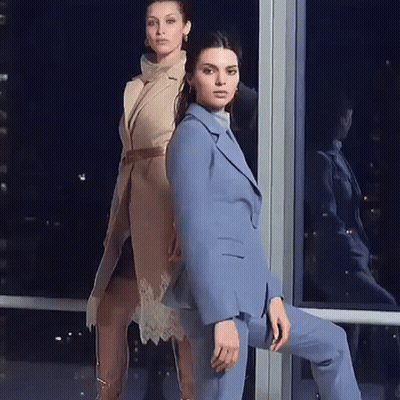 Two Women Are Standing Next To Each Other In Front Of A Window . One Of The Women Is Wearing A Blue Suit . GIF