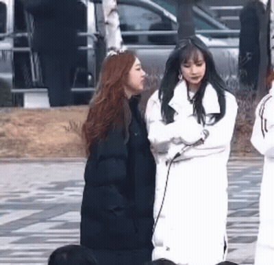 Two Women Are Standing Next To Each Other On A Sidewalk In Front Of A Car . GIF
