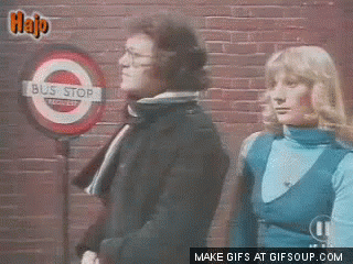 Two Women Are Waiting At A Bus Stop With A Sign That Says Bus Stop GIF