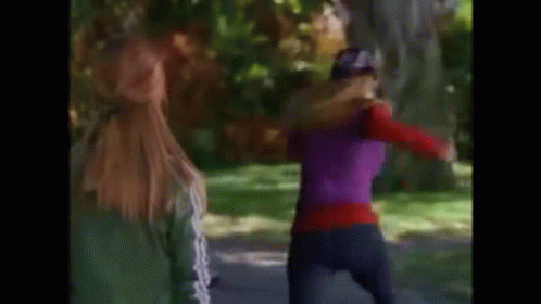 Two Women Are Walking Down A Path In A Park . One Of The Women Is Wearing A Purple Top . GIF