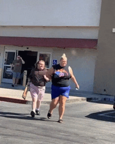 Two Women Are Walking Down The Street In Front Of A Building With A Handicap Sign GIF