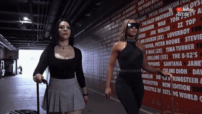 Two Women Are Walking In Front Of A Wall That Has A Youtube Logo On It GIF