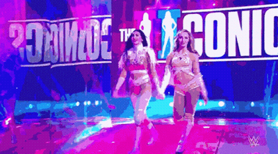 Two Women Are Walking On A Stage In Front Of A Sign That Says ' Iconic ' GIF