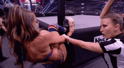 Two Women Are Wrestling In A Ring While A Referee Watches . GIF