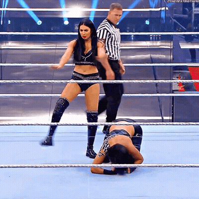 Two Women Are Wrestling In A Ring With A Referee Standing Behind Them GIF
