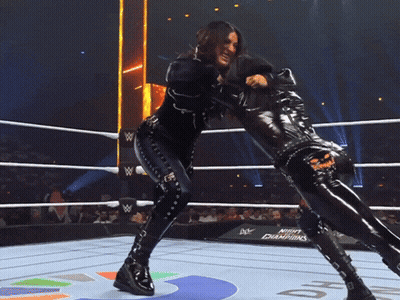 Two Women Are Wrestling In A Ring With A Sign That Says Night Champions In The Background GIF