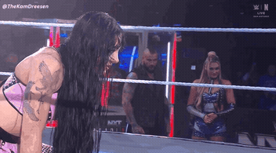 Two Women Are Wrestling In A Wrestling Ring While A Man Stands In The Background . GIF