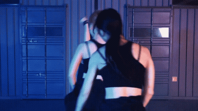 Two Women Dancing In Dark Room With Blue Wall GIF