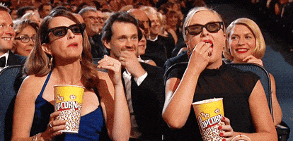Two Women Eating Popcorn While Wearing 3D Glasses In A Theater GIF