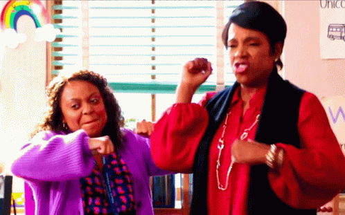 Two Women Flexing Muscles In Front Of Unicorn Sign GIF