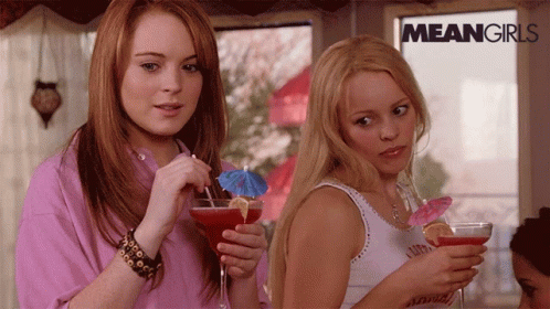 Two Women Holding Drinks in Front of Mean Girls Sign