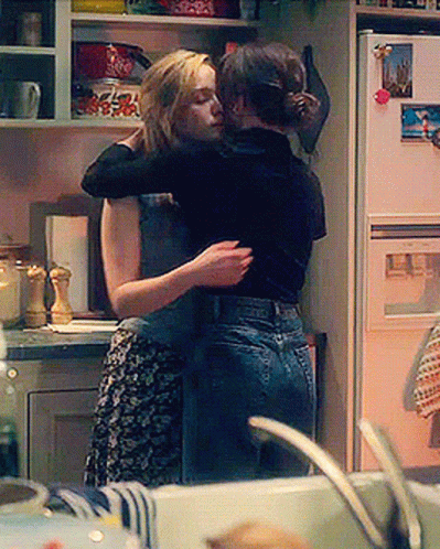 Two Women Hugging In A Kitchen With A Picture Of A City On The Refrigerator Door GIF