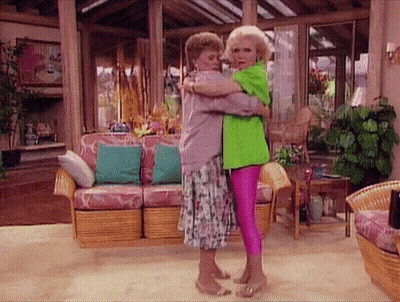 Two Women Hugging In A Living Room With A Couch And Chairs GIF