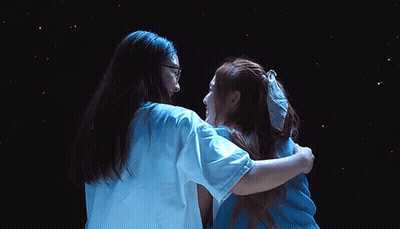 Two Women Hugging In Front Of Dark Background GIF