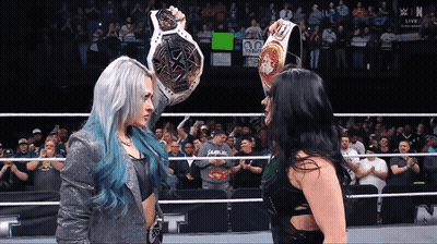 Two Women In A Wrestling Ring With One Holding A Belt That Says Champion GIF