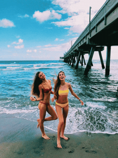 Two Women In Bikinis Are Posing For A Picture On A Beach GIF