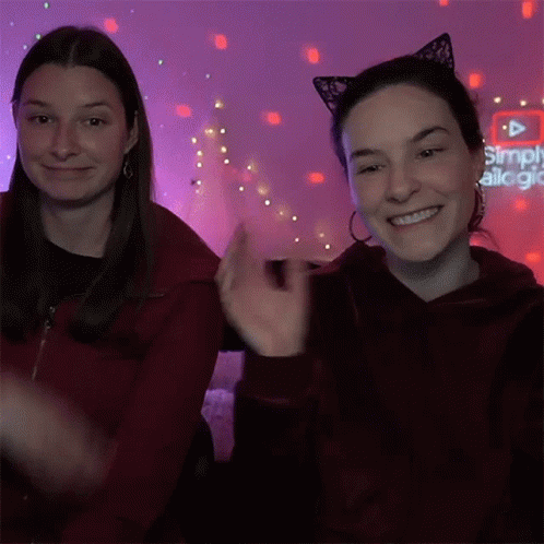 Two Women In Cat Ear Headbands In Front Of Simply Alegria Sign GIF