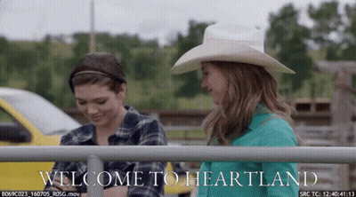 Two Women In Front Of Fence Saying Welcome To Heartland GIF