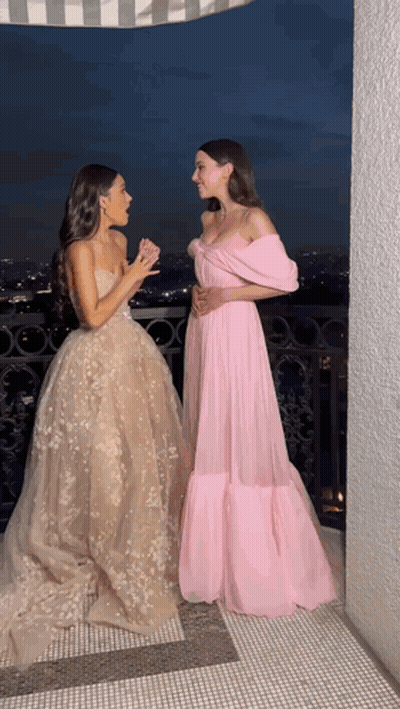 Two Women In Long Dresses Are Standing Next To Each Other On A Balcony At Night GIF