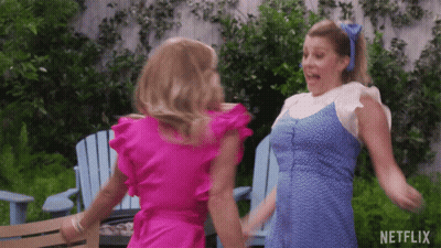 Two Women In Pink And Blue Dresses Are Dancing In Front Of Blue Chairs And A Netflix Logo GIF
