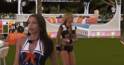 Two Women In Swimsuits Are Standing In A Room With A Couch In The Background GIF