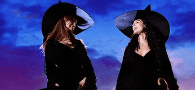 Two Women In Witch Costumes Are Standing Next To Each Other . GIF