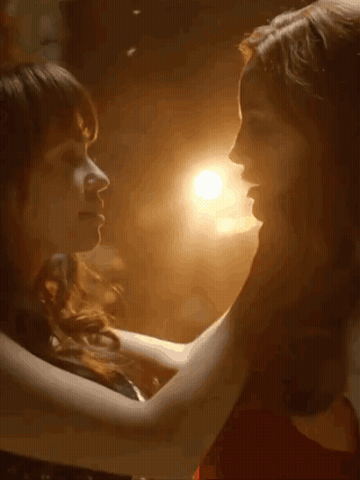 Two Women Kissing In Dark Room With Light Behind Them GIF