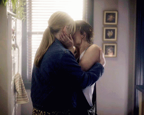 Two Women Kissing In Front Of A Window With Three Pictures On The Wall Behind Them GIF