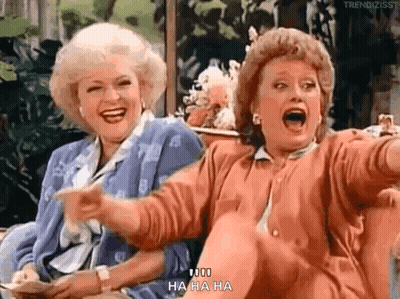 Two Women Laughing And Pointing On Couch GIF