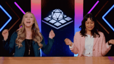 Two Women Laughing With Arms In Air At Table GIF