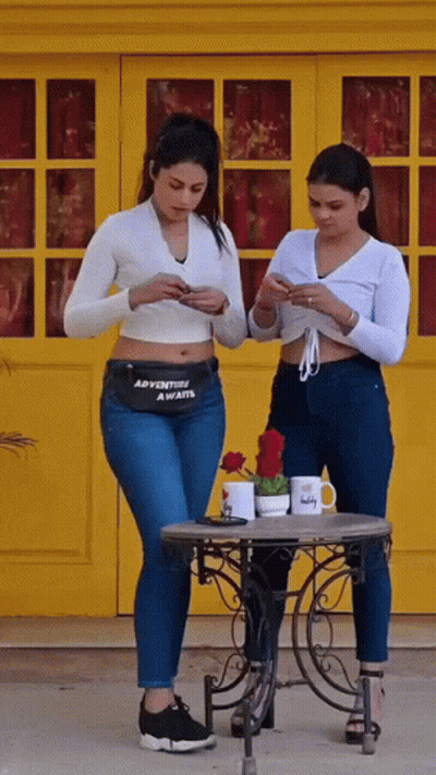 Two Women Looking At Phones With Adventure Awaits Fanny Pack GIF