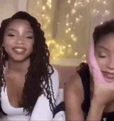 Two Women On Couch One With Pink Glove On Face GIF