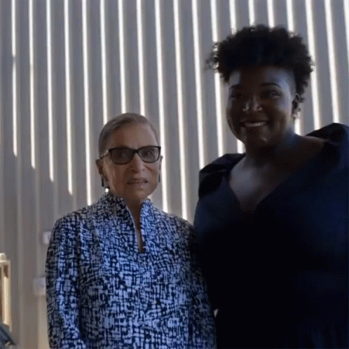 Two Women Posing For A Picture In Front Of A Wall Of Lights GIF