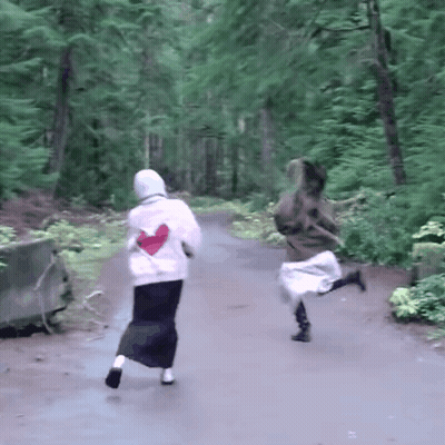 Two Women Running Down Path In Woods One With Heart Shirt GIF