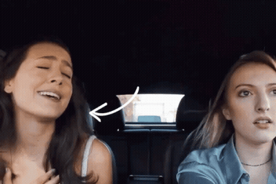 Two Women Singing In Car With Arrow Pointing To Back Window GIF