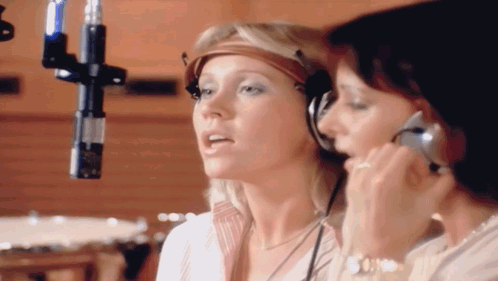 Two Women Singing Into A Microphone With Headphones On GIF