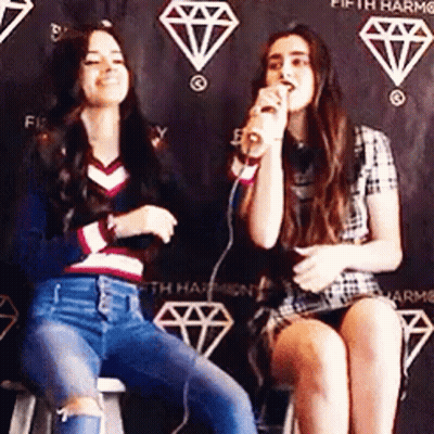 Two Women Singing Into Microphone On Stools GIF
