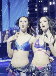 Two Women Singing Into Microphones In Bikini Tops GIF