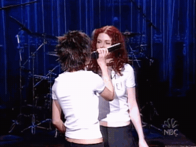 Two Women Singing Into Microphones On Stage GIF